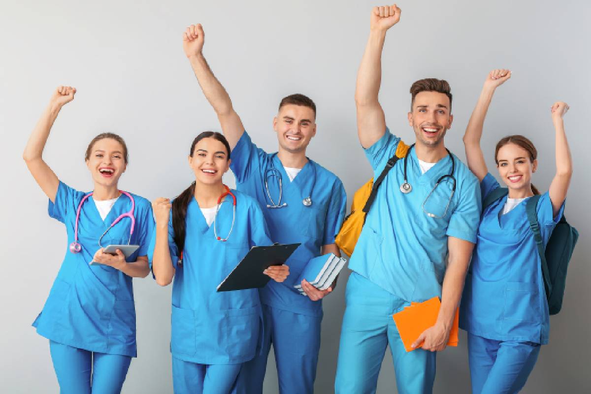 A group of medical assistants in scrubs cheer against a white background near Richmond, Kentucky (KY)